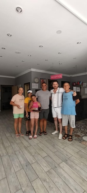 Un grupo de personas en una habitación con una mesa de recepción y un reloj en la pared.