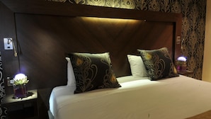 A hotel room with a large bed, two decorative pillows, a nightstand with a lamp, and a wall with an ornate pattern.