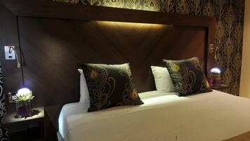 A hotel room with a large bed, two decorative pillows, a nightstand with a lamp, and a wall with an ornate pattern.