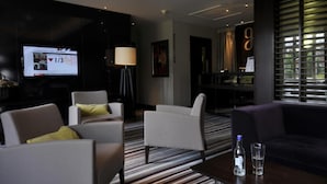 Eine moderne Hotelhalle mit einem Flachbildfernseher, der eine Nachrichtensendung zeigt, einem Empfangsbereich und einer Sitzecke mit Streifenmusterteppich.