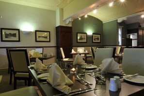 Un comedor con mesas dispuestas para dos, sillas e imágenes enmarcadas en las paredes.