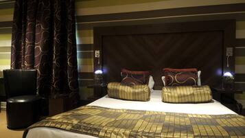 A hotel room with a large bed, two bedside tables, a chair, and a curtain with a wavy pattern.