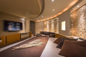 A modern hotel room with a large bed, a flat-screen TV mounted on the wall, a seating area with a sofa and armchairs, and a decorative wall panel. - Hotel C. Chiba Shiroi (Shiroi)