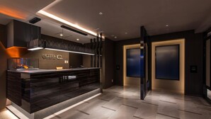 A modern hotel lobby with a reception desk, a fireplace, and a large screen. - Hotel C. Chiba Shiroi (Shiroi)