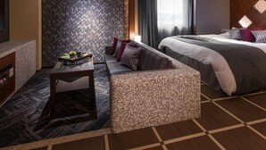 A hotel room with a bed, a sofa, a small table with a tray of fruits, and a patterned wall. - Hotel C. Chiba Shiroi (Shiroi)