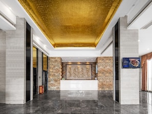 A hotel reception area with a marble reception desk, a golden ceiling, and a stone wall with a relief sculpture. - The BLD International Hotel (Dongguan)