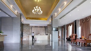 Un vestíbulo de hotel con piso de mármol, una recepción, una araña y un área de estar con un sofá y sillones.