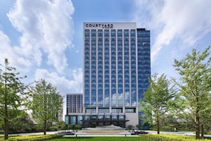 A modern hotel building with a prominent 'Courtyard' sign, surrounded by well-maintained greenery and a clear sky. - Courtyard by Marriott Changchun (Changchun)