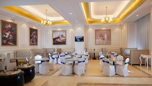 Un comedor de hotel con mesas redondas, sillas blancas y candelabros.