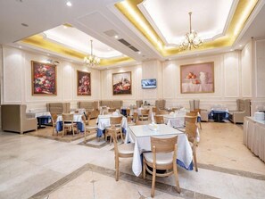 A spacious dining area with multiple tables and chairs, a chandelier, and artwork on the walls. - Venus International Hotel (Dongguan)