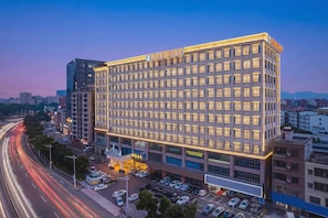 A multi-story hotel with a modern facade, a parking lot, and a busy street with light trails. - Venus International Hotel (Dongguan)