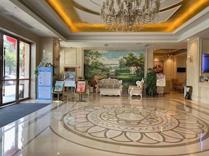 Eine Lobby mit einer Chandelier, einer Wandmalerei, einem Empfangsbereich und einer Sitzecke.
