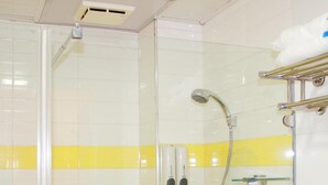 Un espacio de ducha con azulejos amarillos y blancos, una puerta de vidrio, un cabezal de ducha y un perchero para toallas.