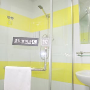 Un baño con una decoración amarilla y blanca, cabina de ducha de vidrio, lavamanos blanco y un letrero de precaución en la pared.