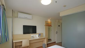 Ein Hotelzimmer mit einem Bett, einem Schreibtisch, einem Flachbildfernseher, einem Stuhl, einer kleinen Mülltonne und einer Tür.