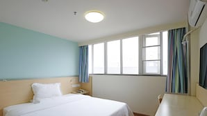Ein Hotelzimmer mit Bett, Nachttisch, Lampe, Fenster mit Vorhängen und Klimaanlage.