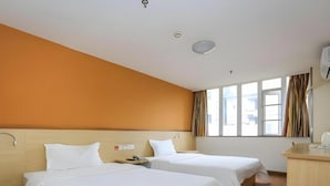 Ein Hotelzimmer mit zwei Betten, einem Holzkopfteil, einem Schreibtisch mit Stuhl und einem Fenster mit Vorhängen.
