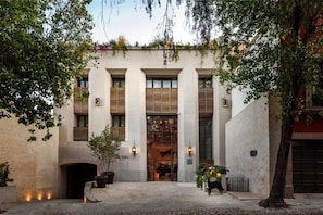 A building with a central entrance, flanked by columns, and a courtyard with potted plants and a tree. - Numu Boutique Hotel (San Miguel de Allende)