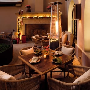 A cozy outdoor dining area with wicker furniture, a table set for two, and a decorative fireplace in the background. - Numu Boutique Hotel (San Miguel de Allende)