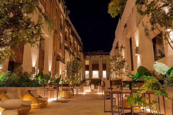 An outdoor seating area with wicker furniture and potted plants, surrounded by buildings with large windows and balconies. - Numu Boutique Hotel (San Miguel de Allende)