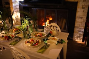 Una mesa de comedor preparada para una comida, con platos de comida, vasos y una chimenea al fondo.