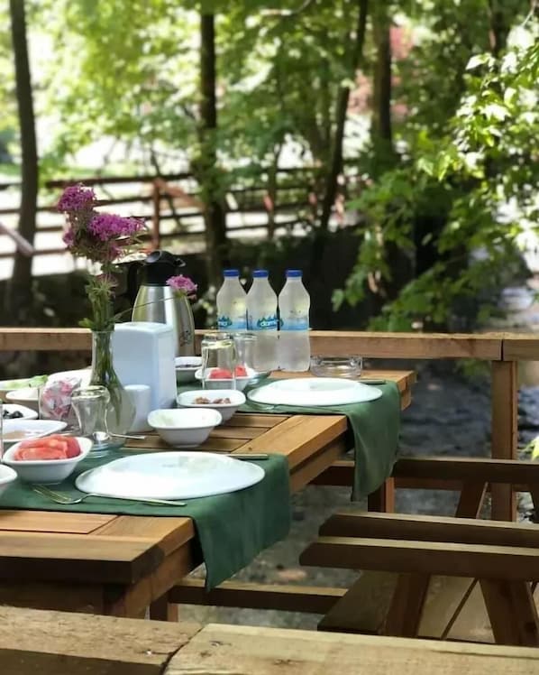 Mesa exterior con vajilla, ensaladeras y botellas, rodeada de sillas.