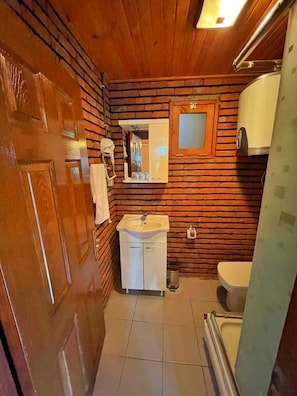 Un baño pequeño con pared de madera, un lavamanos, un inodoro y una zona de ducha.