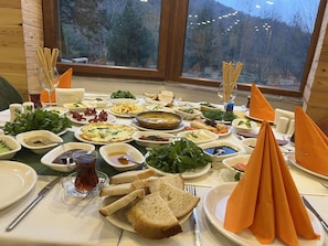 A table set for a meal with various dishes and utensils, a window with a view of trees, and a wooden wall.
