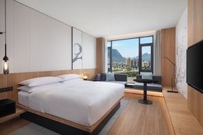 A modern hotel room with a large bed, a seating area, a TV, and a view of a cityscape. - Fairfield by Marriott Bijie (Bijie)