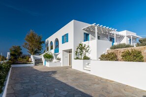 Um edifício branco com persianas azuis, entrada com calçada de pedra e céu azul límpido.