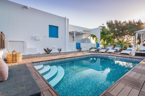 A swimming pool with a tiled edge, a white building with a blue door, and a pergola with blue cushions. - Eiriana Luxury Suites (Milos)