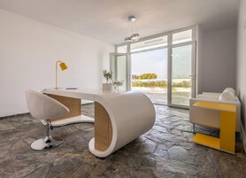 Interior moderno com uma escrivaninha branca curva, uma cadeira, um abajur amarelo e vista através de portas de vidro.