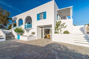 Un bâtiment moderne aux murs blancs, agrémenté de touches de bleu, avec une cour pavée de pierres et un escalier menant à un espace abrité.