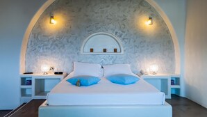 Ein Schlafzimmer mit einem weißen Bett, zwei blauen Kissen, einem weißen Kopfteil und zwei Nachttischen mit Lampen.