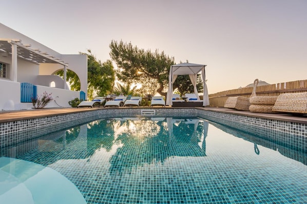 Une piscine avec des chaises longues et un espace salon abrité.