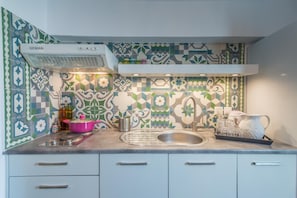 A kitchen with a patterned backsplash, a stainless steel sink, and a pink pot on the counter. - Eiriana Luxury Suites (Milos)