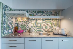 A kitchen with a patterned backsplash, a stainless steel sink, and a pink pot on the counter.