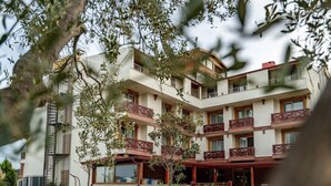 A multi-story hotel with balconies, a covered entrance, and a landscaped garden. - Troya Otel (Ezine)