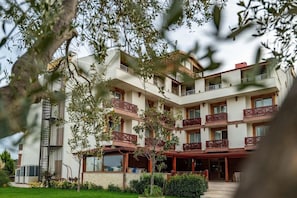 A multi-story hotel with balconies, a covered entrance, and a landscaped garden. - Troya Otel (Ezine)
