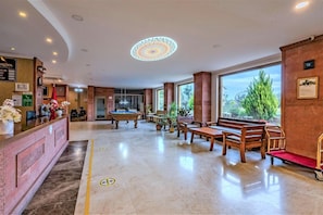 A hotel lobby with a reception desk, pool table, seating area, and large windows. - Troya Otel (Ezine)