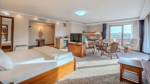 A hotel room with a bed, a desk, a television, and a balcony with chairs. - Troya Otel (Ezine)