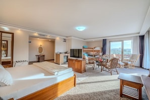 A hotel room with a bed, a desk, a television, and a balcony with chairs. - Troya Otel (Ezine)