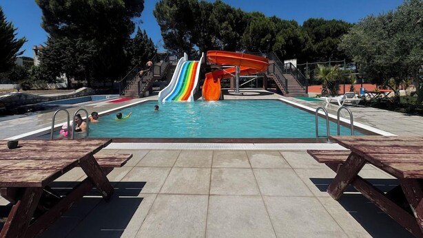 A swimming pool with a multi-colored slide, picnic tables, and a clear sky. - Troya Otel (Ezine)