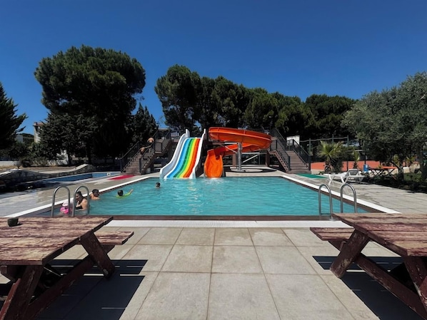 A swimming pool with a multi-colored slide, picnic tables, and a clear sky. - Troya Otel (Ezine)