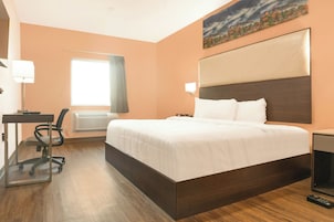 Quarto de hotel com uma cama grande, uma escrivaninha com cadeira, janela com cortinas e um quadro na parede.
