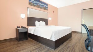 A hotel room with a large bed, a nightstand with a phone and alarm clock, a desk with a chair, and a painting on the wall. - OYO Hotel Adairsville Calhoun South I-75 (Adairsville)