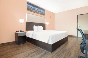 A hotel room with a large bed, a nightstand with a phone and alarm clock, a desk with a chair, and a painting on the wall. - OYO Hotel Adairsville Calhoun South I-75 (Adairsville)