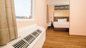 A hotel room with a bed, a window, a radiator, and a painting on the wall. - OYO Hotel Adairsville Calhoun South I-75 (Adairsville)