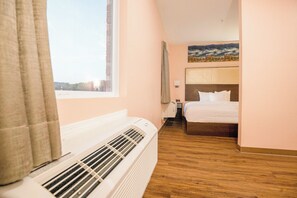 A hotel room with a bed, a window, a radiator, and a painting on the wall. - OYO Hotel Adairsville Calhoun South I-75 (Adairsville)