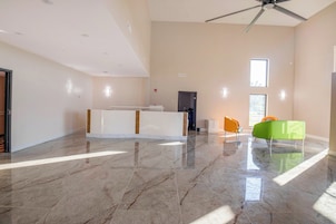 Um quarto amplo com piso de mármore, balcão de recepção, ventilador de teto e janela que garante iluminação natural.